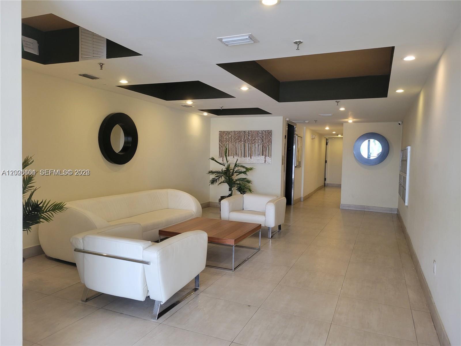 A modern lobby features white leather seating, a wooden coffee table, and recessed ceiling panels — 2924 Collins Ave # 301, Miami Beach FL 33140, MIAMI BEACH, FL