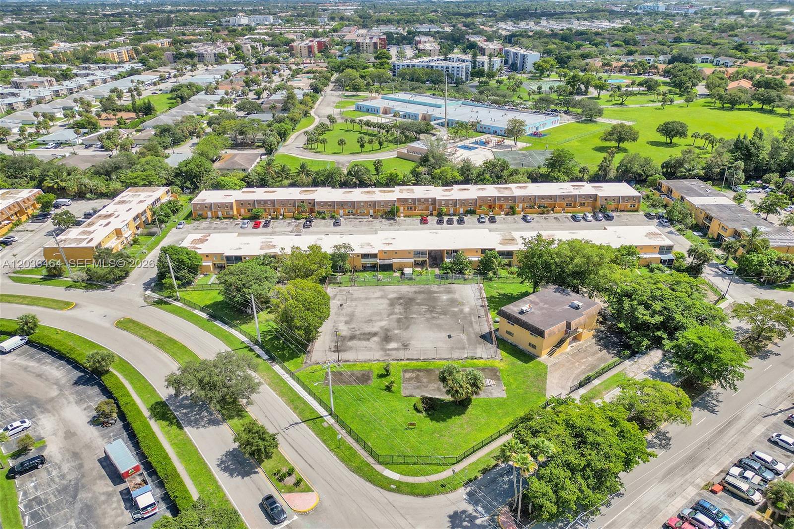 An aerial view shows multi-story apartment buildings, a fenced sports court, and surrounding parking lots — 2600 NW 60th Ter, Sunrise FL 33313, SUNRISE, FL