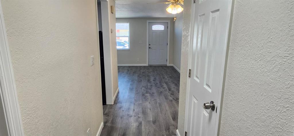 A hallway with light-colored walls and gray wood-look flooring leads toward an exterior door — 5000 BITNER STREET, NEW PORT RICHEY, FL