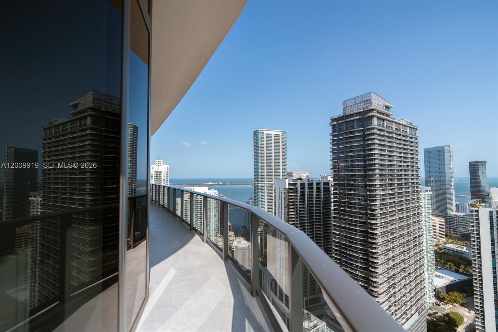 A high-rise balcony with a glass railing overlooks a city skyline and the ocean — 45 SW 9th St # 4906, Miami FL 33130, MIAMI, FL