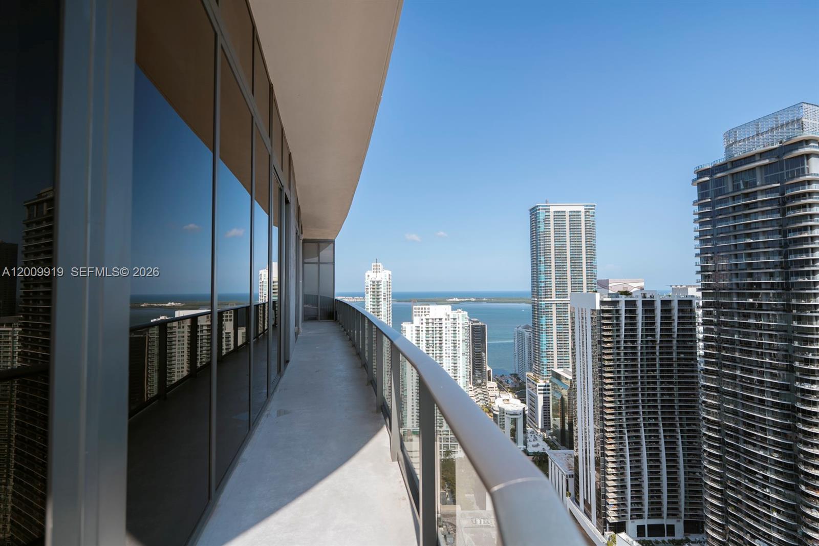 A high-rise balcony with a glass railing overlooks a city skyline and the ocean — 45 SW 9th St # 4906, Miami FL 33130, MIAMI, FL