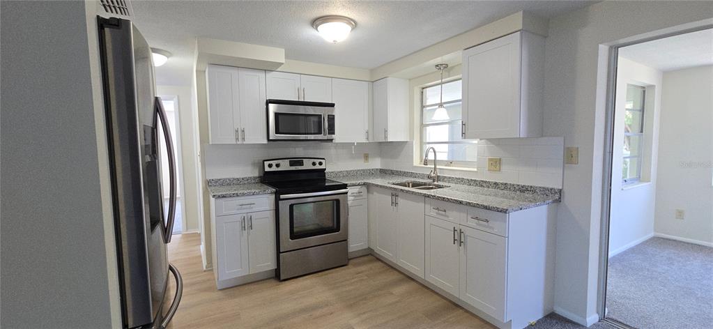 A kitchen features white cabinets, stainless steel appliances, granite countertops, and light wood-look flooring — 4102 DALWOOD DRIVE, HOLIDAY, FL