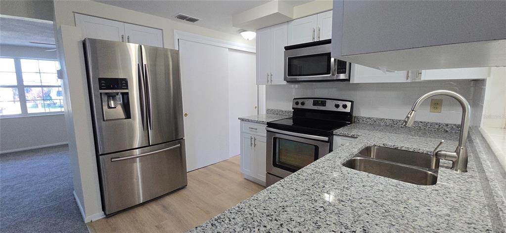 A kitchen features stainless steel appliances, white cabinets, and speckled granite countertops — 4102 DALWOOD DRIVE, HOLIDAY, FL