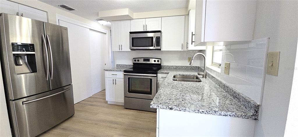 A kitchen features stainless steel appliances, white cabinets, and speckled granite countertops — 4102 DALWOOD DRIVE, HOLIDAY, FL