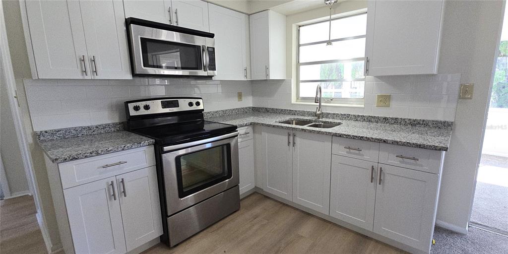 A kitchen features white cabinets, stainless steel appliances, granite countertops, and a subway tile backsplash — 4102 DALWOOD DRIVE, HOLIDAY, FL