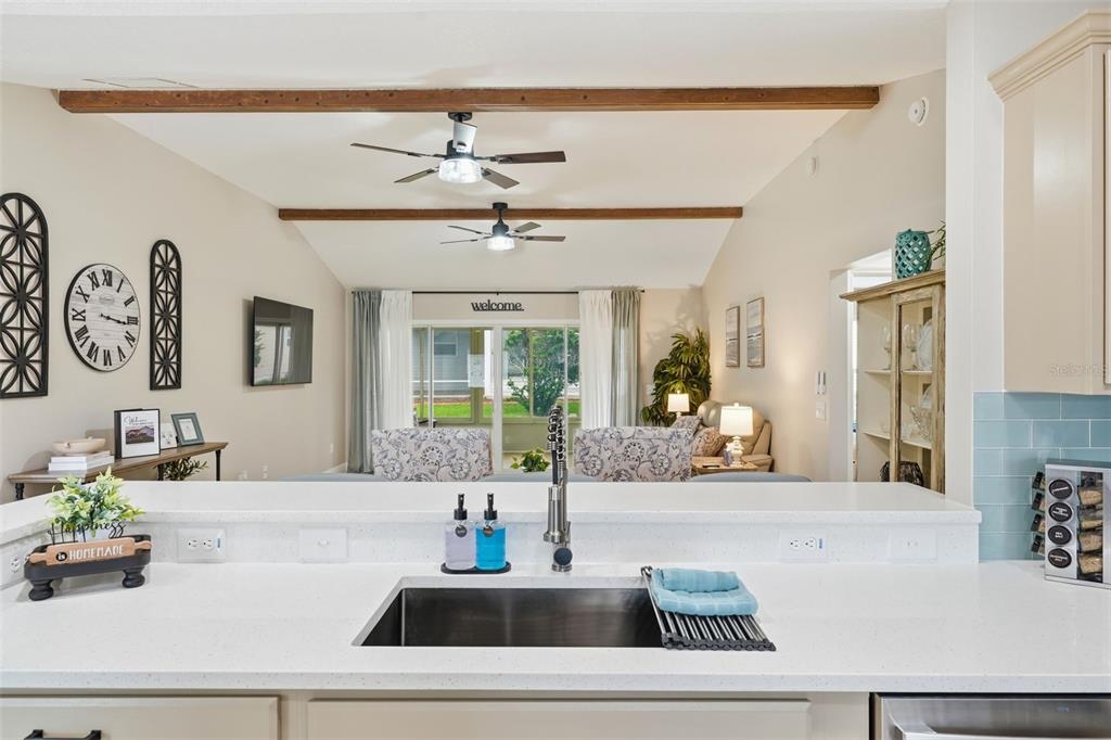 A kitchen sink overlooks a living room with vaulted ceilings, exposed beams, and ceiling fans — 17173 SE 79TH MCLAWREN TERRACE, THE VILLAGES, FL