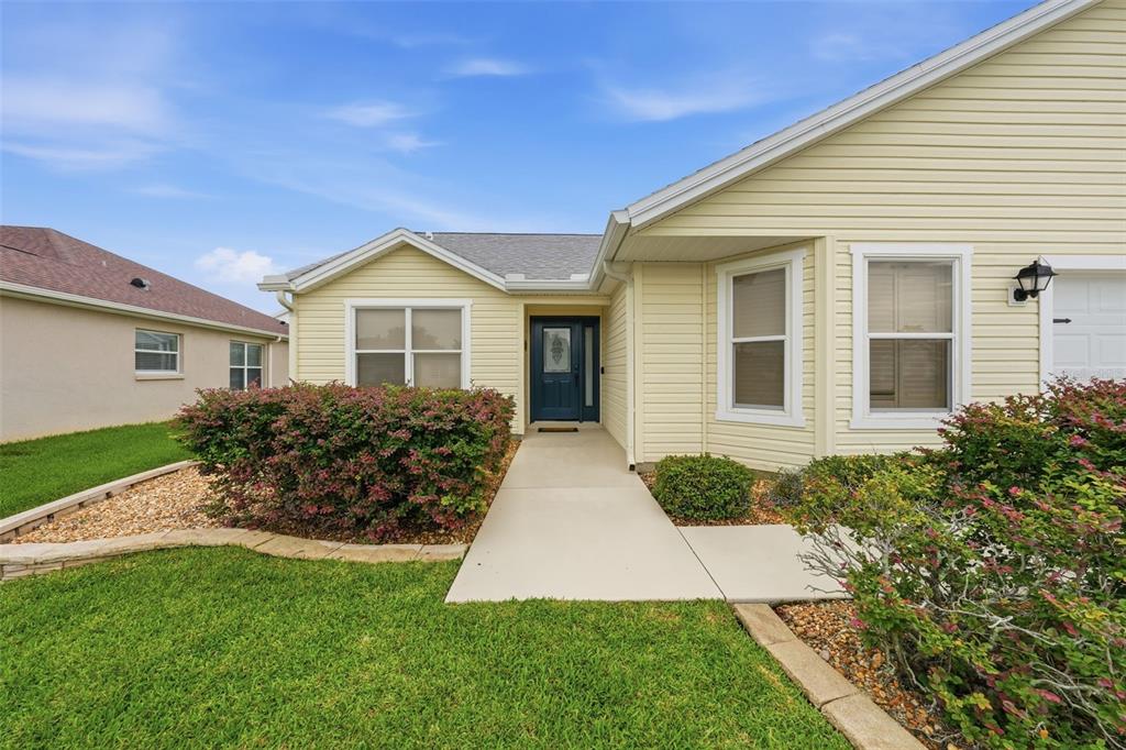 A light yellow house with a concrete walkway leading to a dark blue front door — 17173 SE 79TH MCLAWREN TERRACE, THE VILLAGES, FL