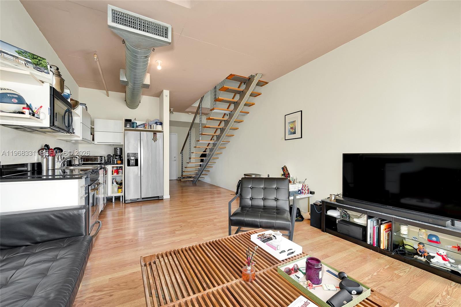 An open-concept living room and kitchen area features hardwood floors, a staircase, and industrial ductwork — 690 SW 1st Ct # 1504, Miami FL 33130, MIAMI, FL