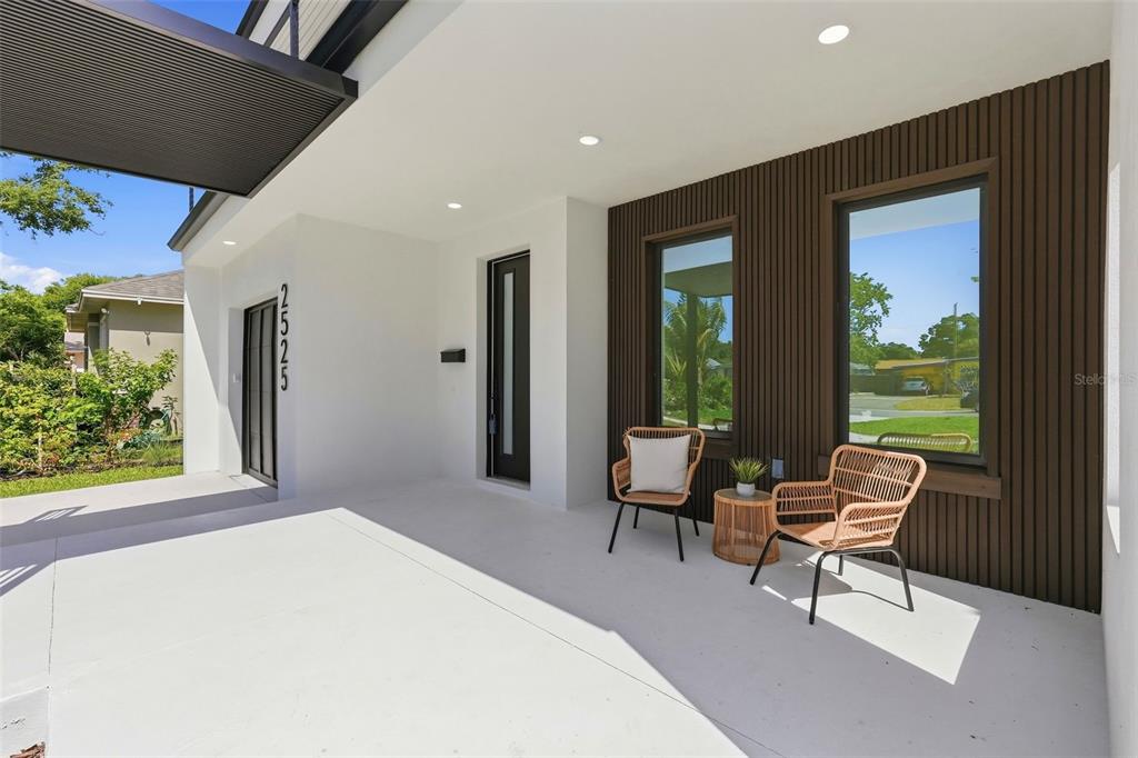 A modern covered porch features white concrete flooring, dark wood-slatted siding, and two wicker chairs — 2525 18TH AVENUE N, ST PETERSBURG, FL