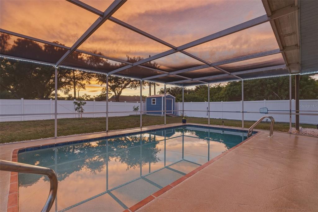 A screened-in swimming pool sits in a backyard with a white fence and storage shed — 342 AURORA STREET, PORT CHARLOTTE, FL