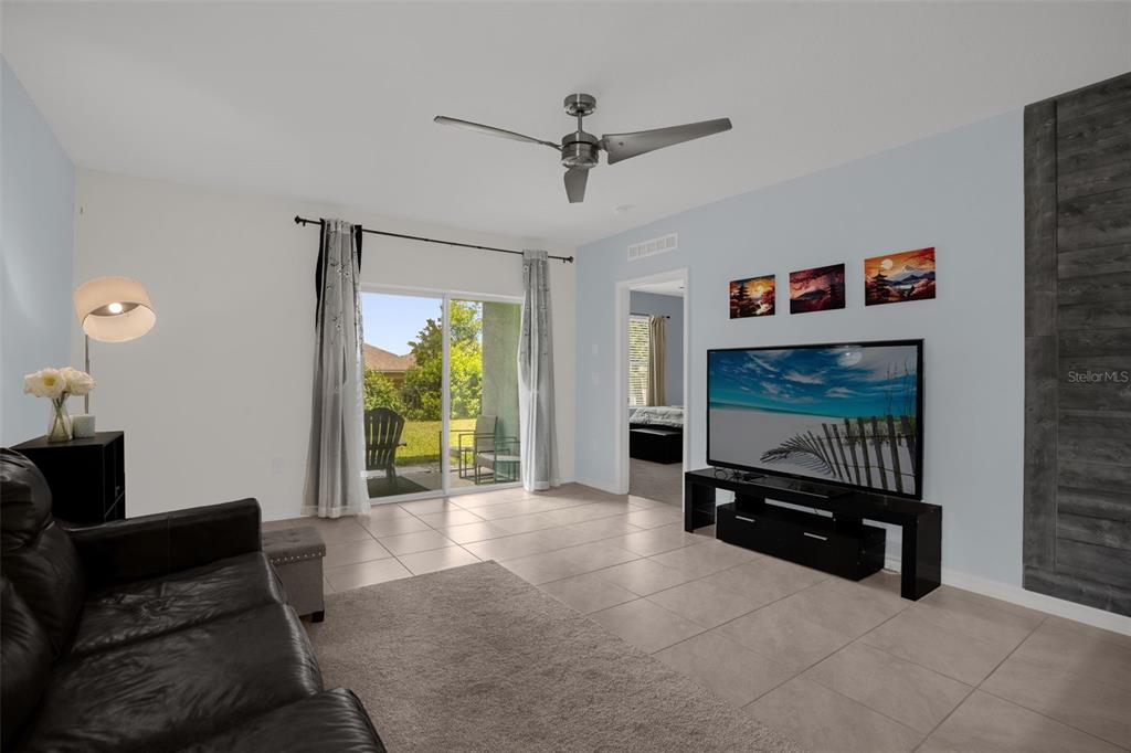A living room with tile floors, a ceiling fan, a television, and a sliding glass door — 334 CHARLES DRIVE, DELAND, FL