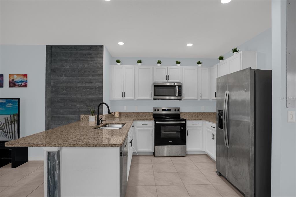A kitchen features white cabinets, granite countertops, stainless steel appliances, and a gray accent wall — 334 CHARLES DRIVE, DELAND, FL