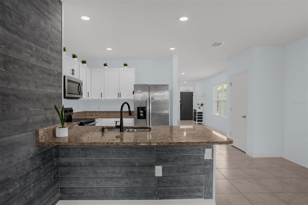 A kitchen features a granite-topped breakfast bar with gray wood-plank siding and white cabinets — 334 CHARLES DRIVE, DELAND, FL