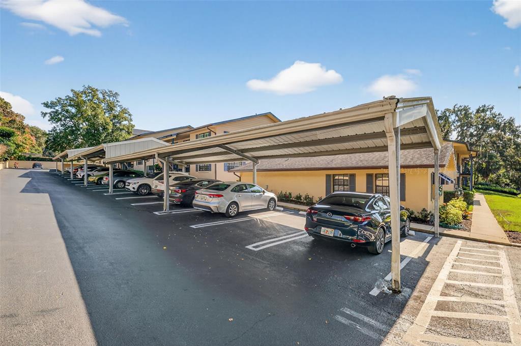 A row of covered parking spaces sits beside a multi-story apartment building — 110 N TREMAIN ST UNIT 105, MOUNT DORA, FL