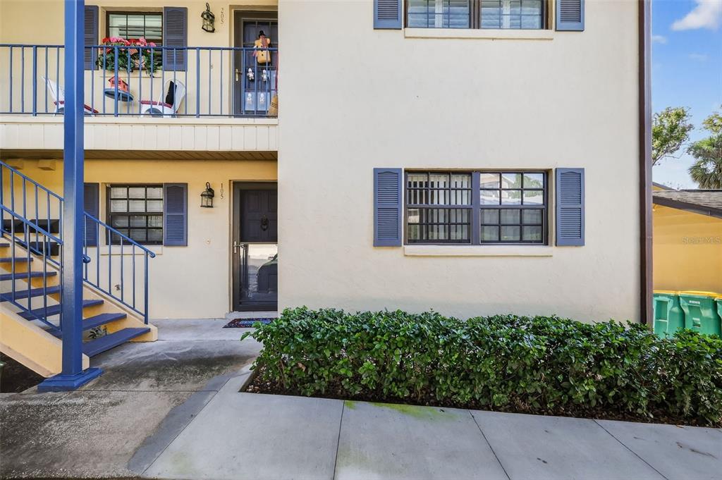 A two-story apartment building exterior features blue metal stairs, balconies, and dark-framed windows — 110 N TREMAIN ST UNIT 105, MOUNT DORA, FL