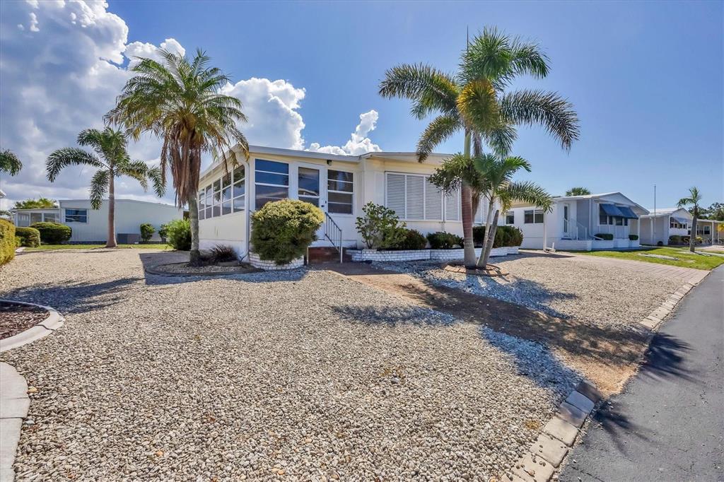 A single-story manufactured home features a gravel yard, palm trees, and a screened-in front porch — 14 S FLORA VISTA STREET, ENGLEWOOD, FL