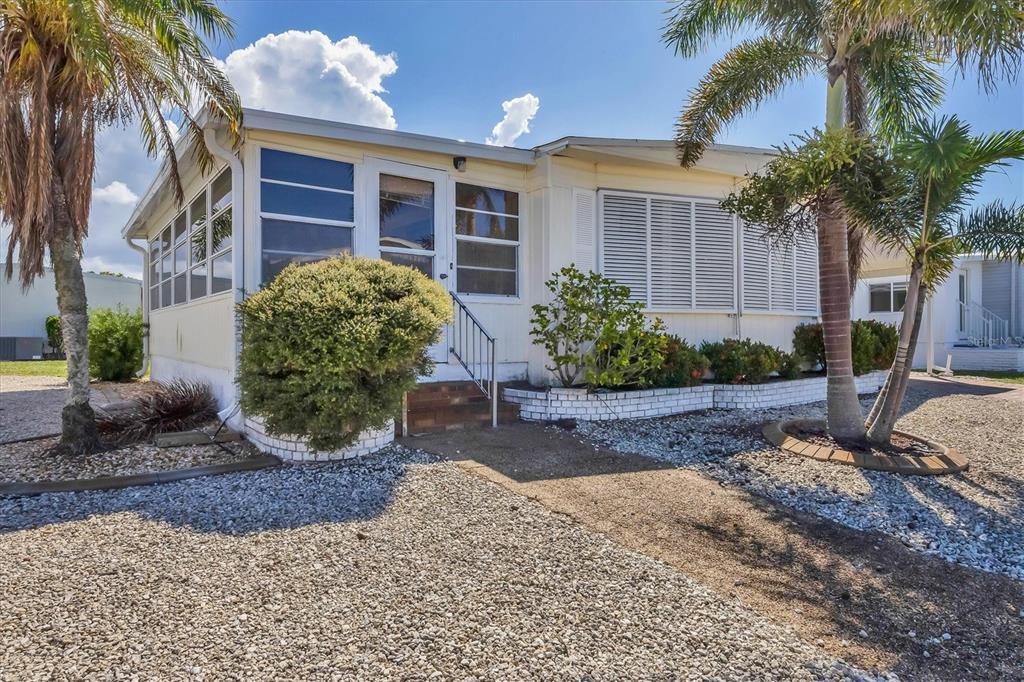 A single-story manufactured home with a screened-in porch, gravel yard, and palm trees — 14 S FLORA VISTA STREET, ENGLEWOOD, FL