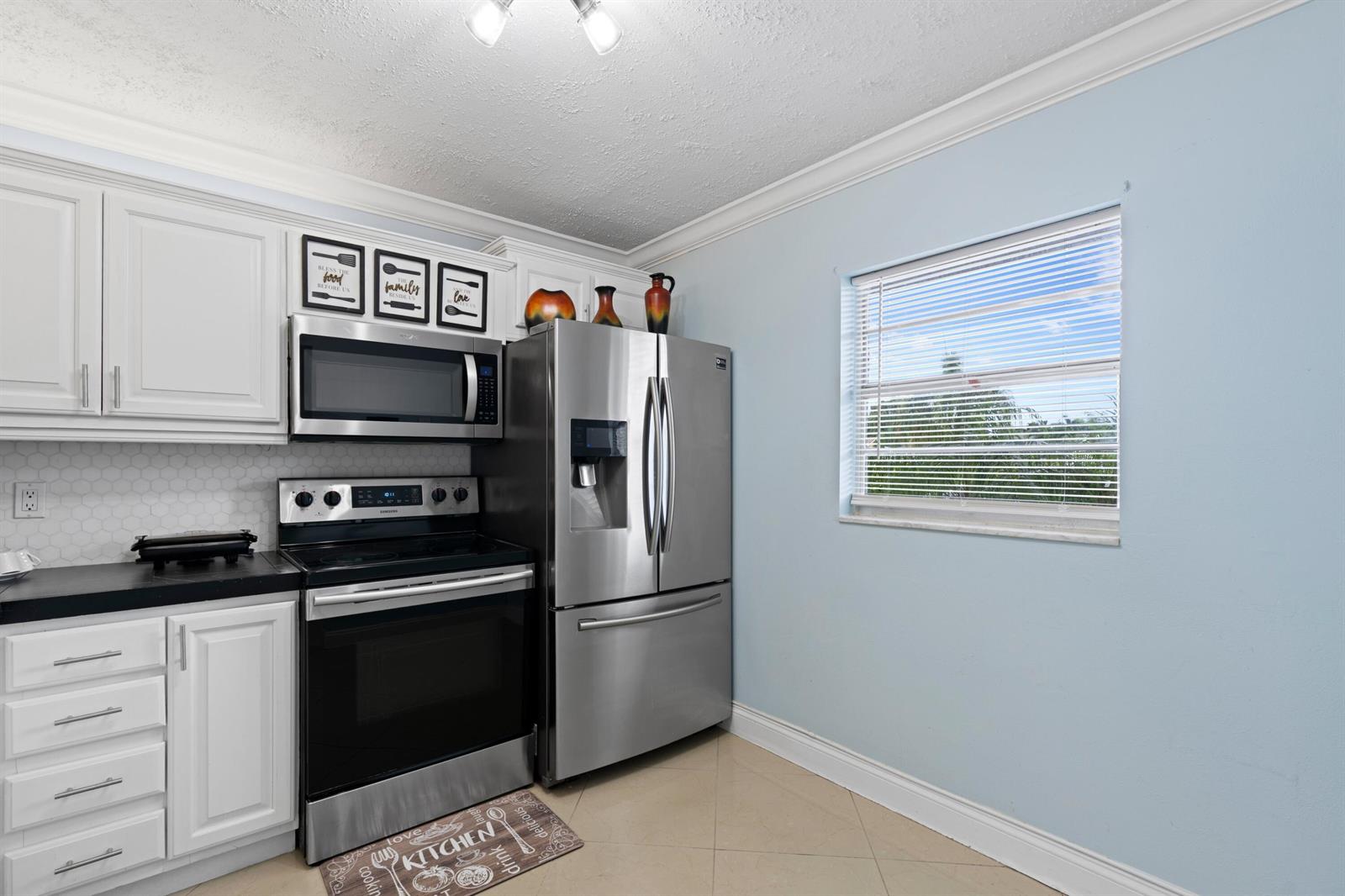 A kitchen features white cabinets, stainless steel appliances, a light blue wall, and tiled flooring — 300 NE 26th Avenue # 1030, Boynton Beach FL 33435, BOYNTON BEACH, FL