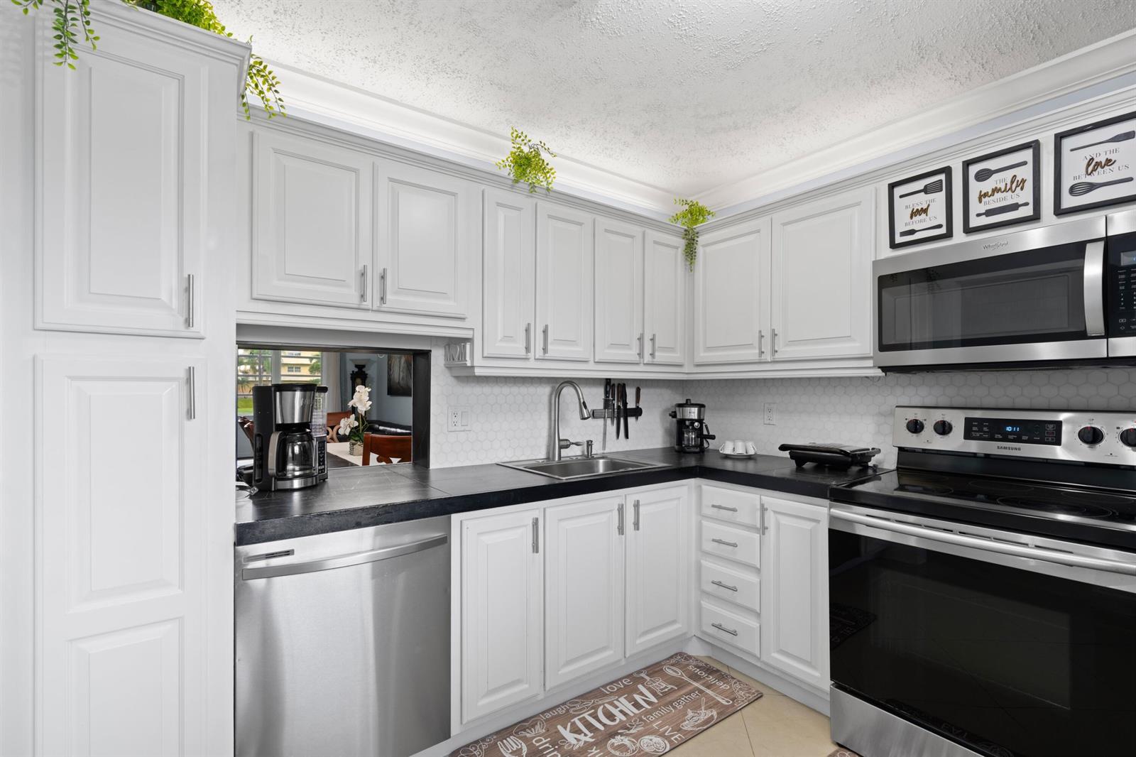 A kitchen with white cabinets, stainless steel appliances, black countertops, and a white backsplash — 300 NE 26th Avenue # 1030, Boynton Beach FL 33435, BOYNTON BEACH, FL