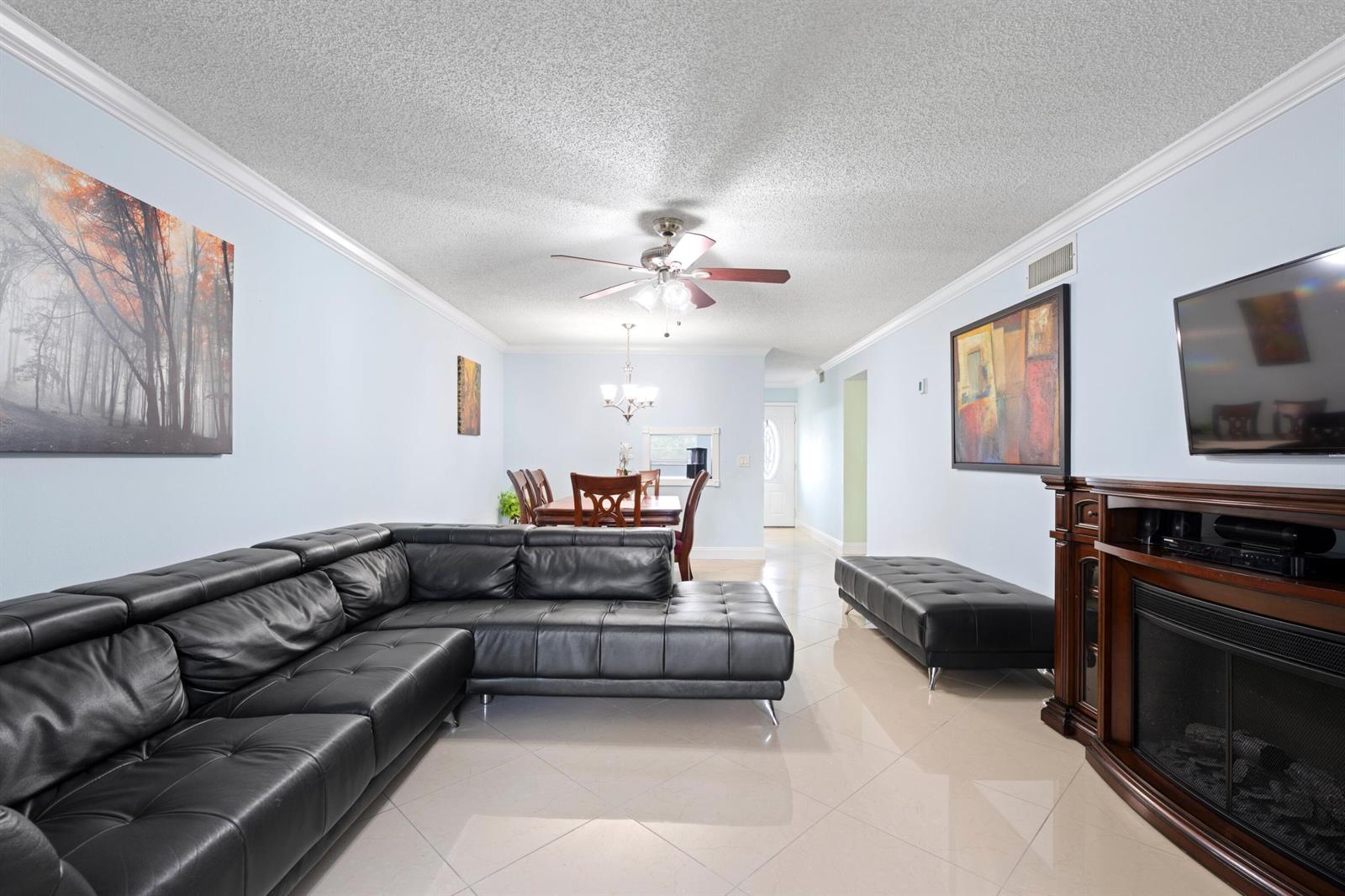 A living room with a black sectional sofa, tiled floors, and a fireplace with TV — 300 NE 26th Avenue # 1030, Boynton Beach FL 33435, BOYNTON BEACH, FL