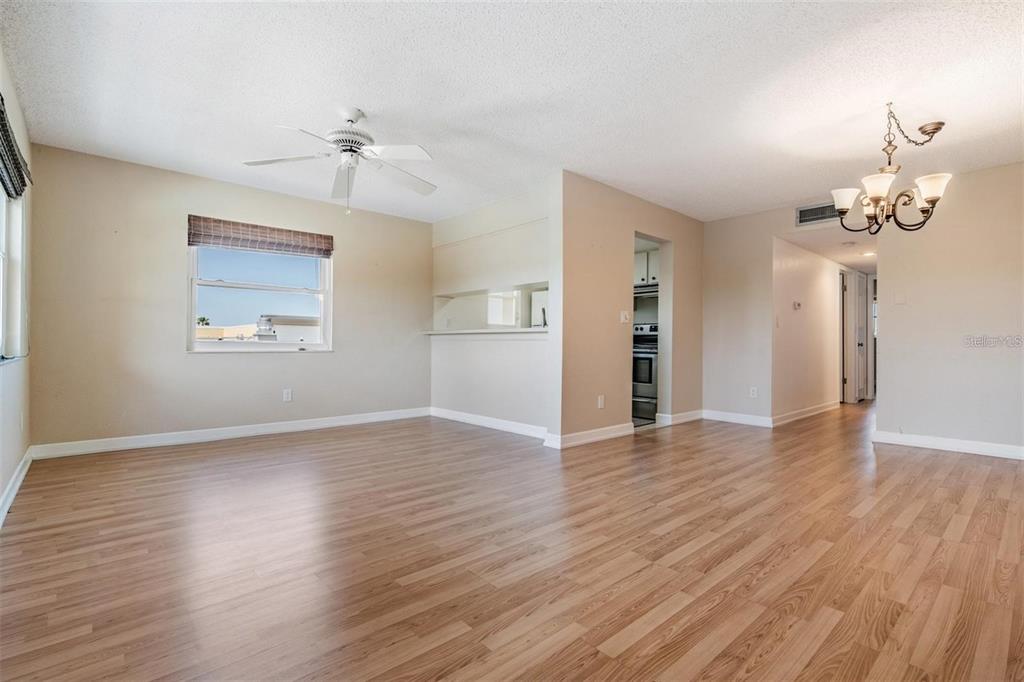 A living room with light wood-look flooring, a ceiling fan, and a pass-through kitchen window — 2525 WEST BAY DRIVE UNIT B44, BELLEAIR BLUFFS, FL
