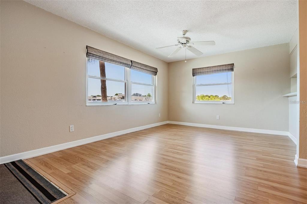 An empty room with light wood-look flooring, beige walls, two windows, and a ceiling fan — 2525 WEST BAY DRIVE UNIT B44, BELLEAIR BLUFFS, FL