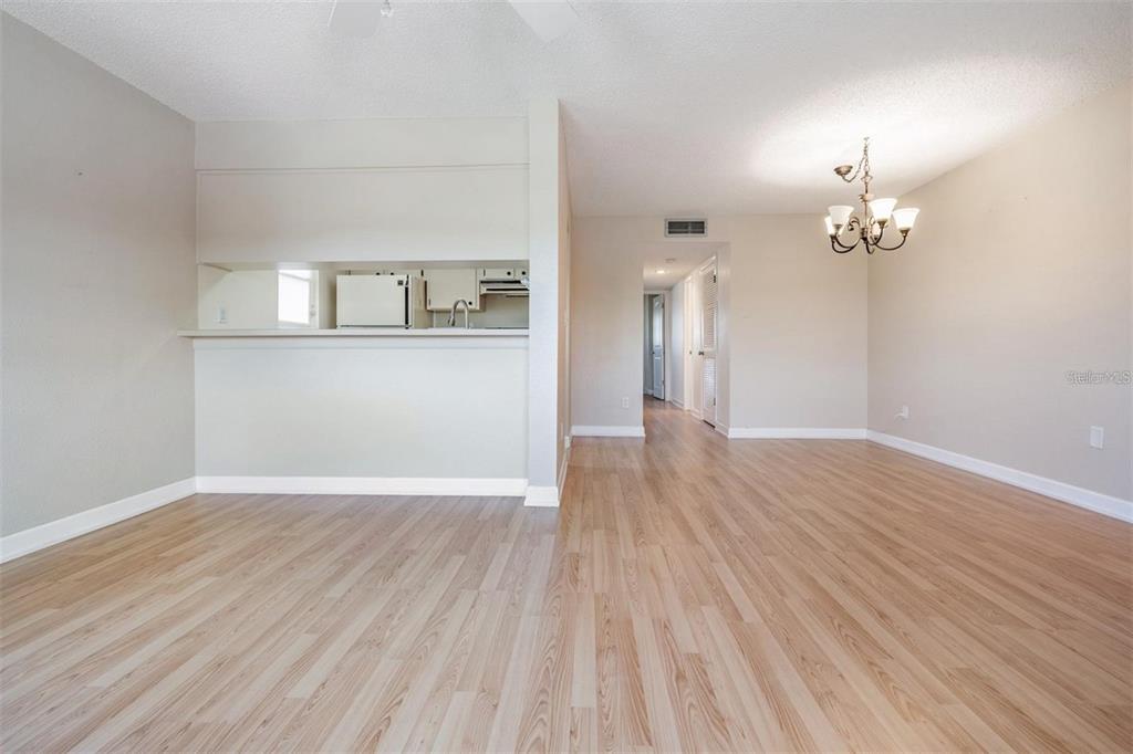 A living and dining area with light wood-look flooring, a kitchen pass-through, and a chandelier — 2525 WEST BAY DRIVE UNIT B44, BELLEAIR BLUFFS, FL