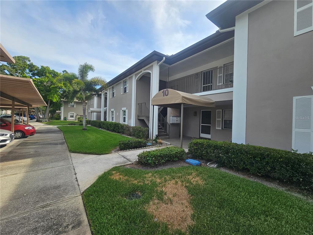 A two-story apartment building exterior features a tan facade, a covered entrance, and parking — 5265 E BAY DRIVE UNIT 1013, CLEARWATER, FL