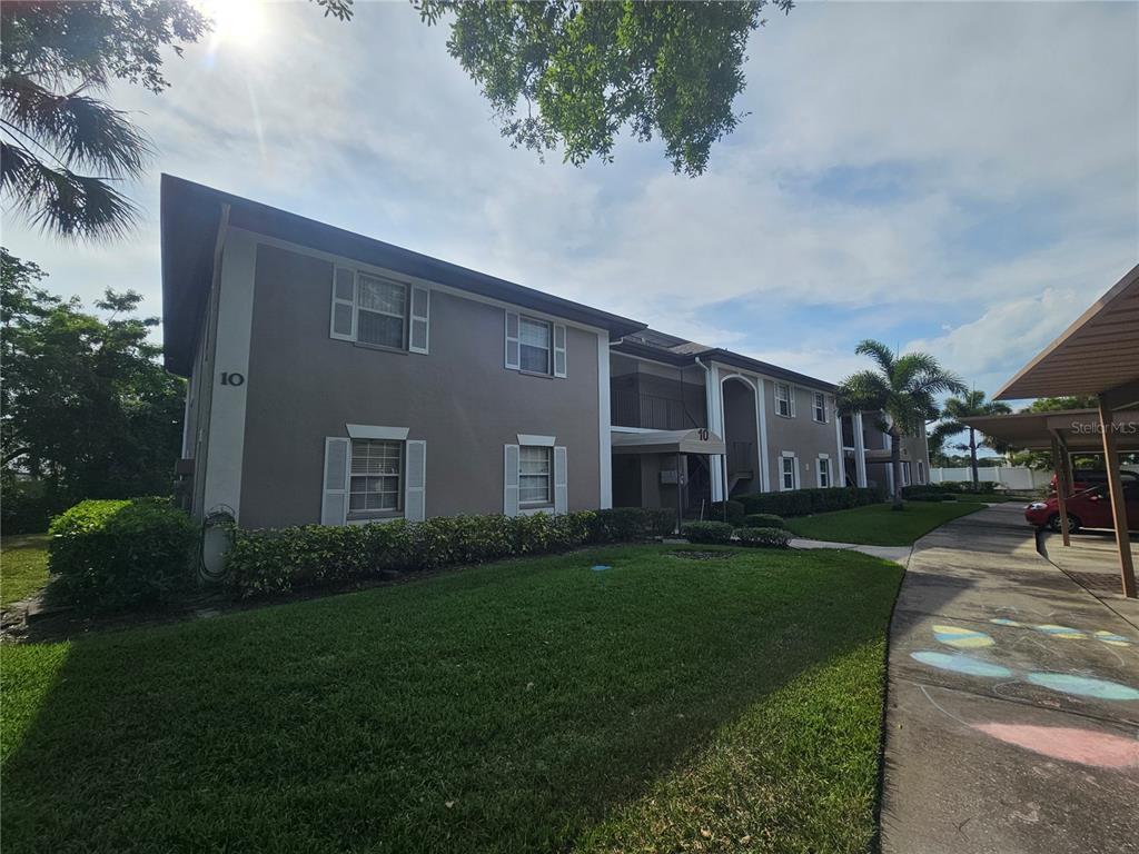 A two-story apartment building with a tan exterior, white shutters, and a covered parking area — 5265 E BAY DRIVE UNIT 1013, CLEARWATER, FL