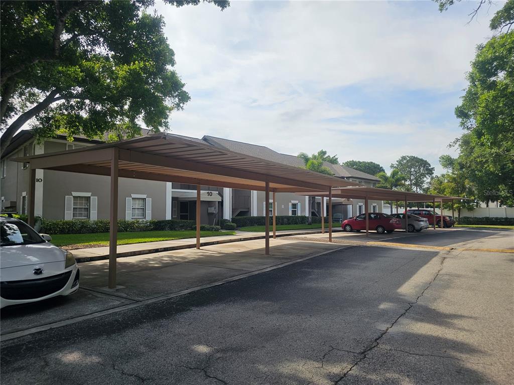 A parking lot with a metal carport structure in front of a multi-story apartment building — 5265 E BAY DRIVE UNIT 1013, CLEARWATER, FL