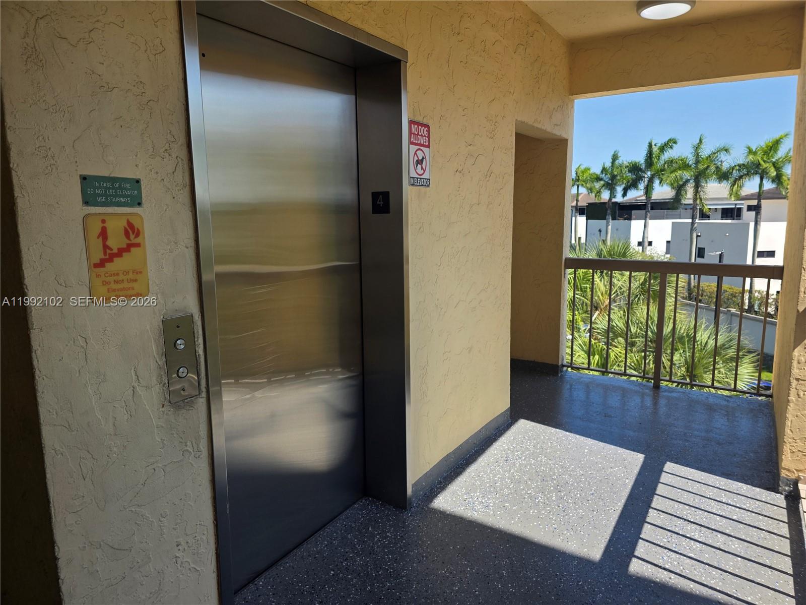 An elevator door is located on a balcony with a metal railing and palm trees — 8100 Geneva Ct # 432, Doral FL 33166, DORAL, FL