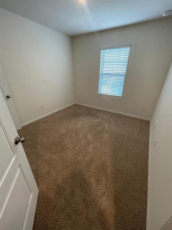 An empty bedroom features beige carpet, off-white walls, and a single window with blinds — 12411 BOWES BRANCH ROAD, ORLANDO, FL