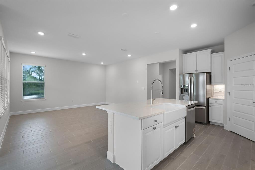 A kitchen island with a farmhouse sink sits in front of a spacious living area — 11857 SHINE VIEW LANE, WINTER GARDEN, FL