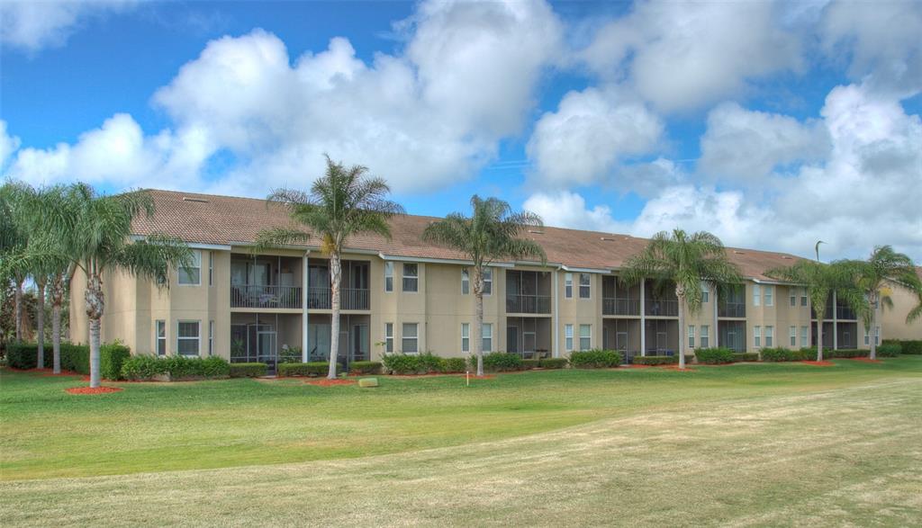 A three-story apartment building with tan stucco walls and screened balconies sits on a lawn — 905 FAIRWAY COVE LANE UNIT 205, BRADENTON, FL