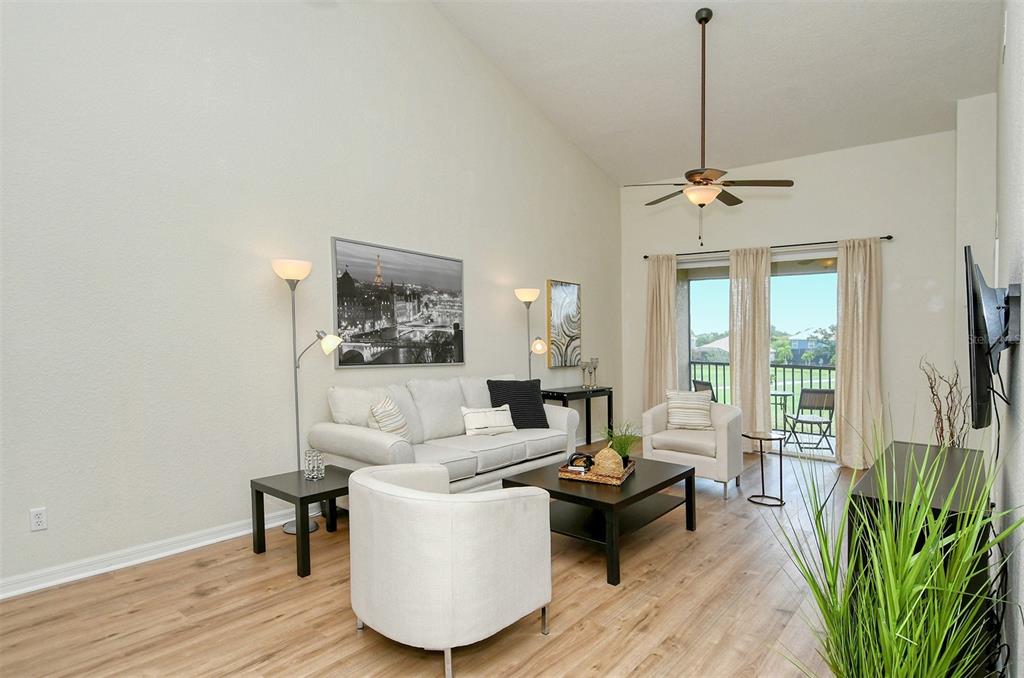 A living room with light wood floors, a vaulted ceiling, and a sliding glass door — 905 FAIRWAY COVE LANE UNIT 205, BRADENTON, FL