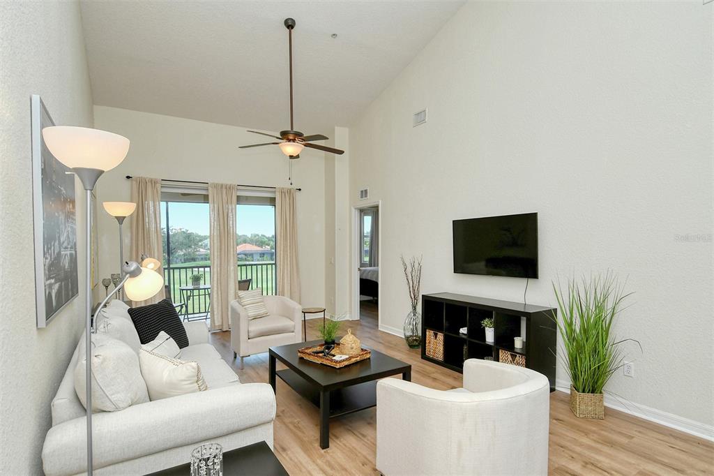 A living room features a white sofa, two armchairs, a coffee table, and a wall-mounted television — 905 FAIRWAY COVE LANE UNIT 205, BRADENTON, FL