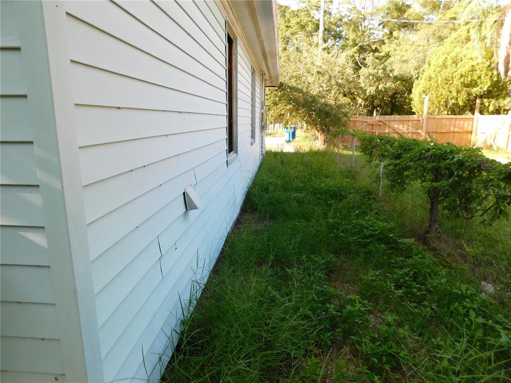 A side view of a white-sided house with tall grass and a wooden fence — 510 6TH AVENUE NW, LARGO, FL
