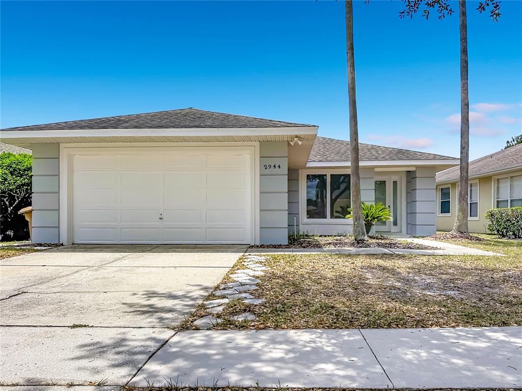 A single-story house with a white garage door, light gray siding, and a concrete driveway — 2944 SUNSET VISTA BOULEVARD, KISSIMMEE, FL