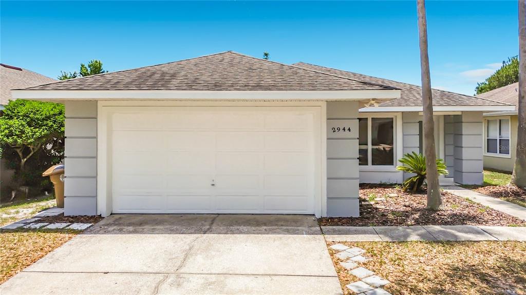 A single-story house with a white garage door, gray siding, and a brown shingled roof — 2944 SUNSET VISTA BOULEVARD, KISSIMMEE, FL
