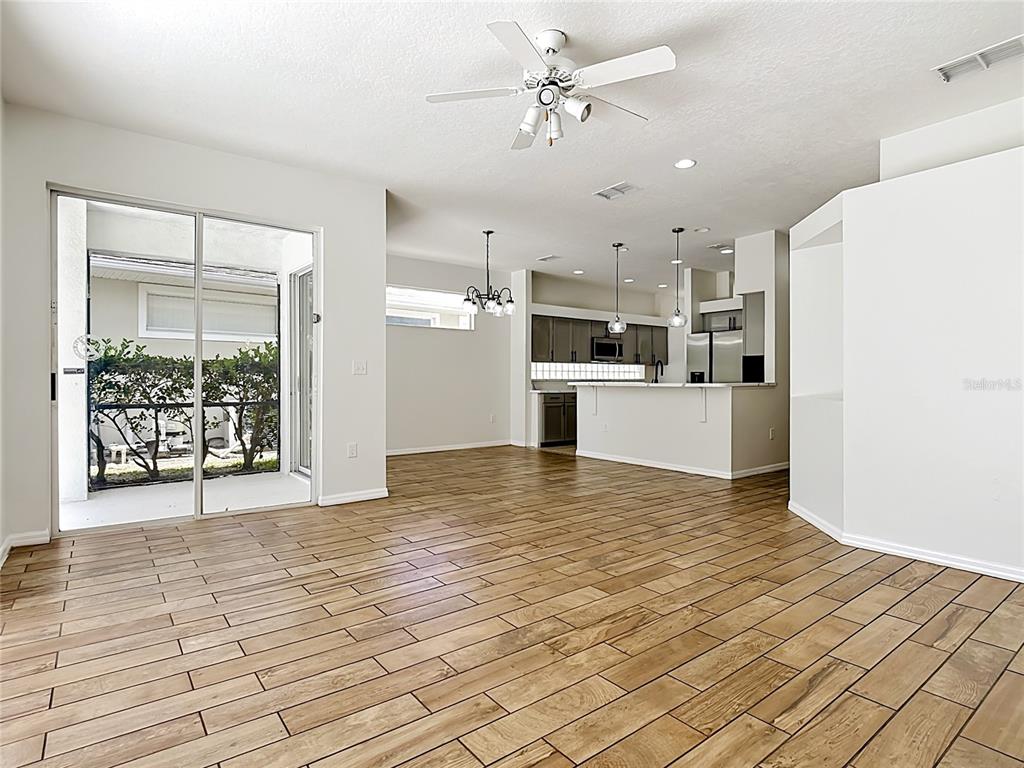 An open-concept living area features wood-look tile flooring, a kitchen island, and sliding glass doors — 2944 SUNSET VISTA BOULEVARD, KISSIMMEE, FL
