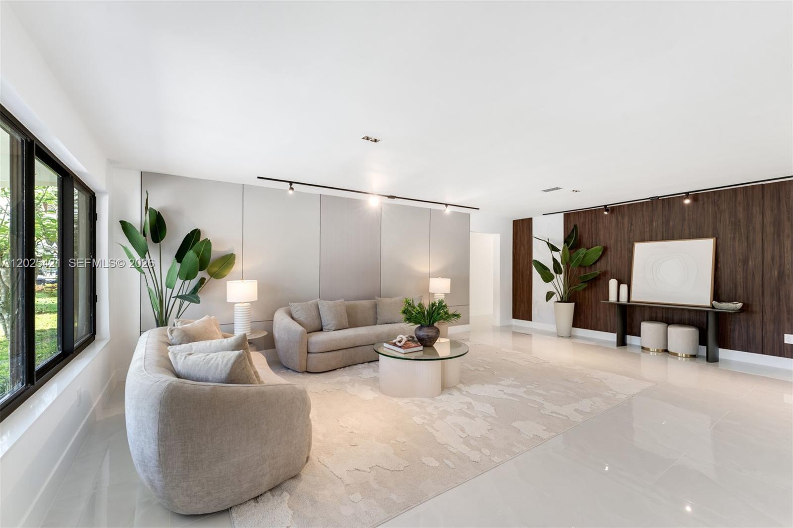A modern living room features two beige sofas, a glass coffee table, and wood paneling — 10825 SW 80th Ave, Miami FL 33156, MIAMI, FL