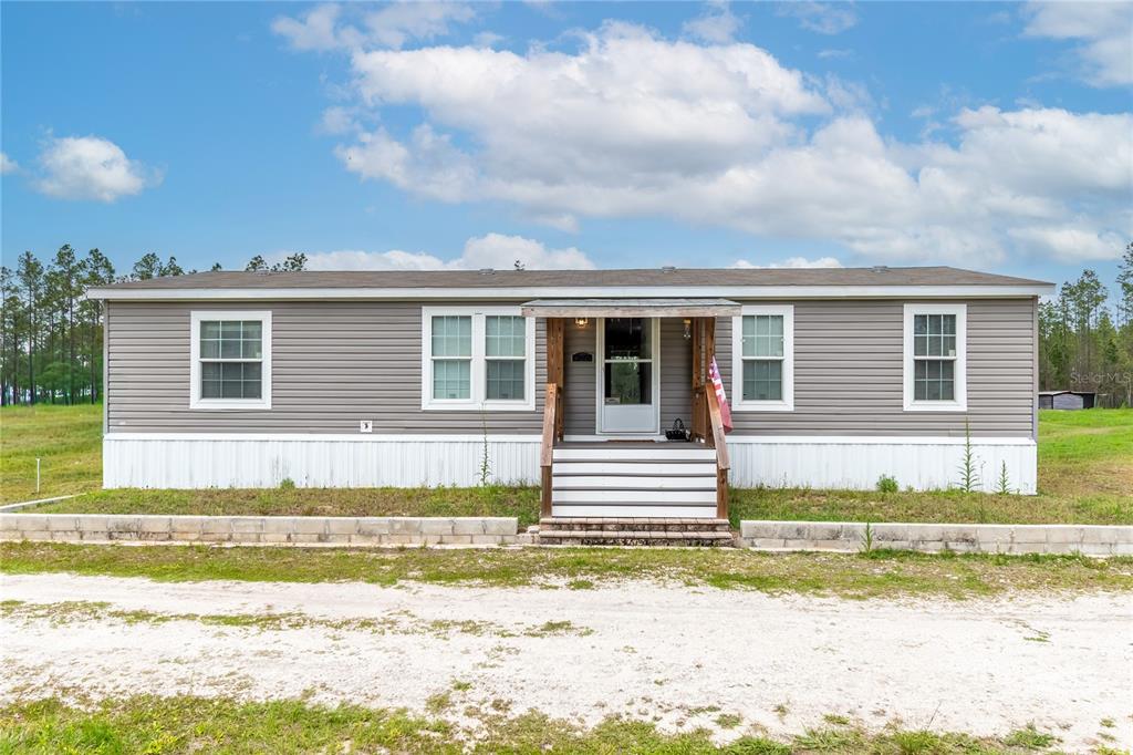 A single-story manufactured home with grey siding and a front porch sits on a lot — 12655 NE 215TH STREET, FORT MC COY, FL