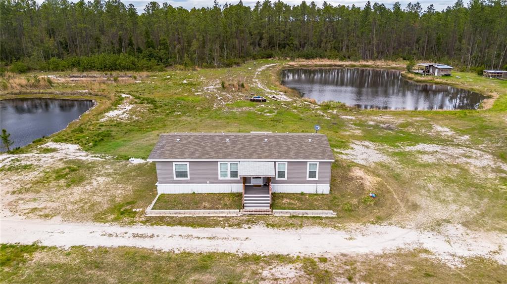 An aerial view shows a house and two ponds surrounded by a dense forest at sunset — 12655 NE 215TH STREET, FORT MC COY, FL