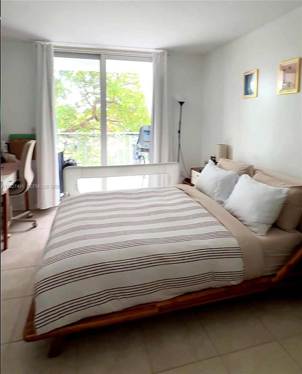 A bedroom features a bed with a striped duvet, a desk, and a sliding glass door — 650 NE 64th St # G402, Miami FL 33138, MIAMI, FL