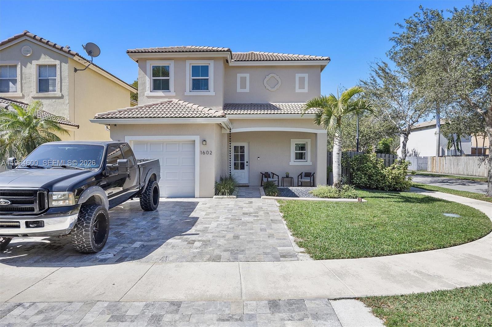 A two-story beige house with a tiled roof, paver driveway, and a black pickup truck — 1602 SE 20th Rd, Homestead FL 33035, HOMESTEAD, FL