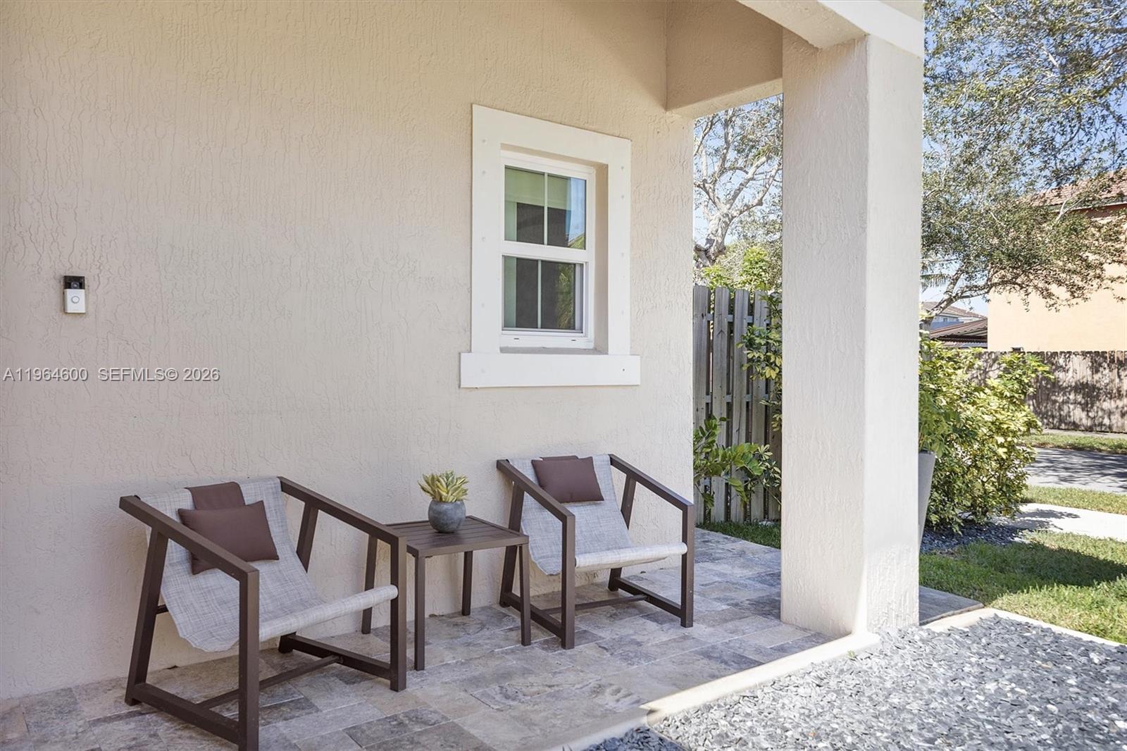 A covered patio features two chairs, a small table, and a window on a stucco wall — 1602 SE 20th Rd, Homestead FL 33035, HOMESTEAD, FL