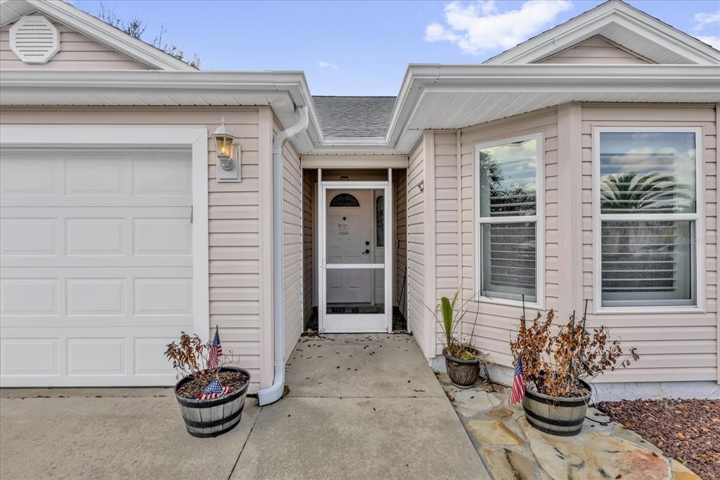The exterior of a light-colored house features a garage, a front entryway, and potted plants — 1462 PELICAN PATH, THE VILLAGES, FL