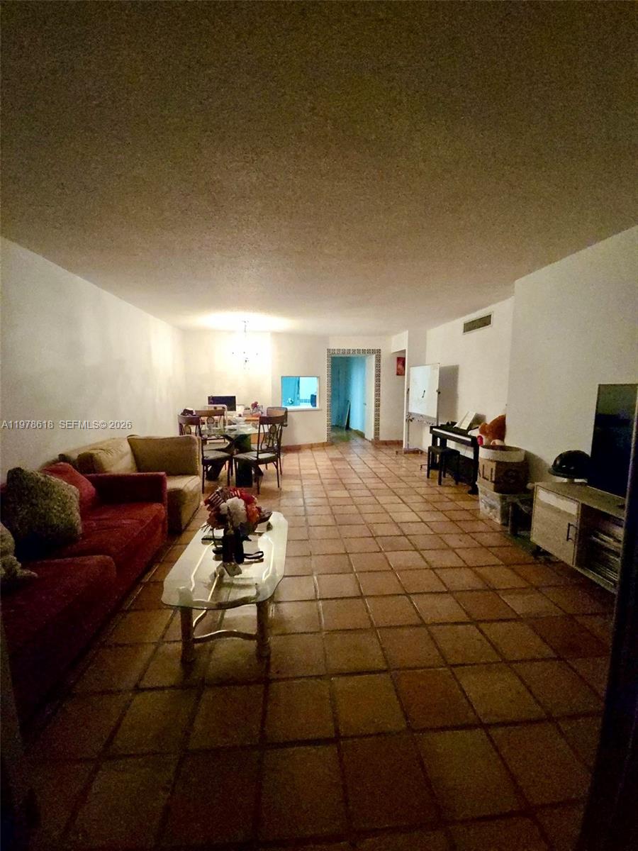 An empty room features terracotta tile flooring, a chandelier, and a pass-through window — 1750 NE 191st St # 3, Miami FL 33179, MIAMI, FL