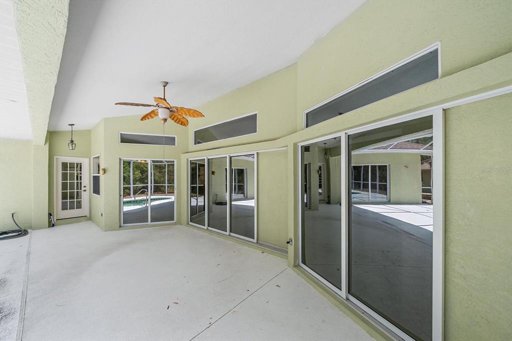 A covered patio features light green walls, sliding glass doors, and a ceiling fan — 630 OLD ENGLEWOOD ROAD, ENGLEWOOD, FL