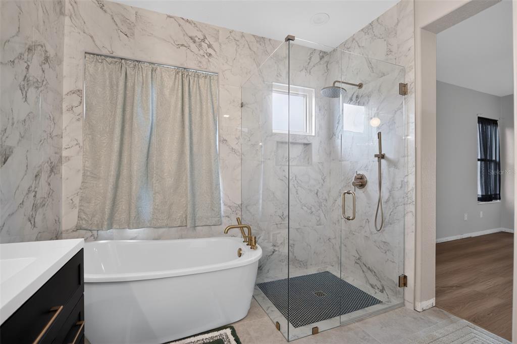 A bathroom features a freestanding tub, a glass-enclosed shower with marble tile, and gold fixtures — 9415 SE 125TH STREET, SUMMERFIELD, FL